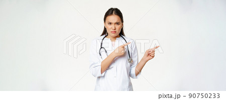 Angry female doctor, asian physician in medical robe and stethoscope, pointing fingers right and frowning furious, staring disappointed, white background Angry female doctor, asian physician in medical robe and stethoscope, pointing fingers right and frowning furious, staring disappointed, white background 90750233