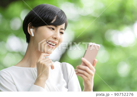 スマホで音楽を聴く若い女性　スマホを操作する若い女性　屋外 90752276