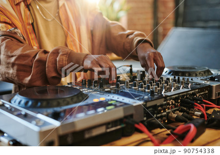Hands of black man regulating sounds on dj set while turning mixers Hands of black man regulating sounds on dj set while turning mixers 90754338