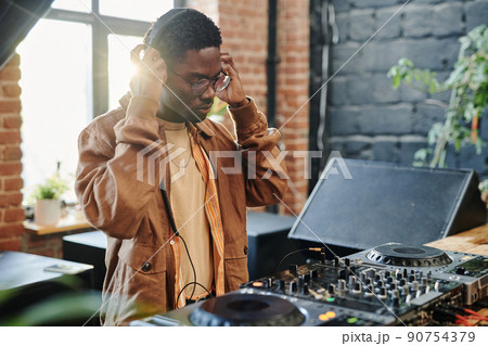 Young black man putting headphones on his head in front of turntables Young black man putting headphones on his head in front of turntables 90754379
