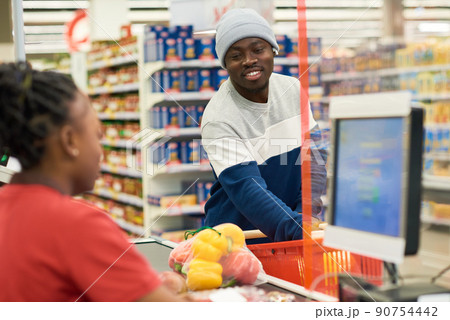 Happy young man in casualwear putting food products on counter line Happy young man in casualwear putting food products on counter line 90754442