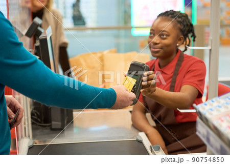 Modern man paying for goods by credit card while holding it by payment terminal Modern man paying for goods by credit card while holding it by payment terminal 90754850