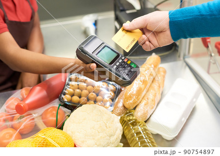 Male consumer holding credit card over payment terminal and food products 90754897