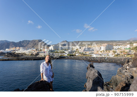 Young smiling woman near volcanic rocks on a city and ocean background. Young smiling woman near volcanic rocks on a city and ocean background. 90755999