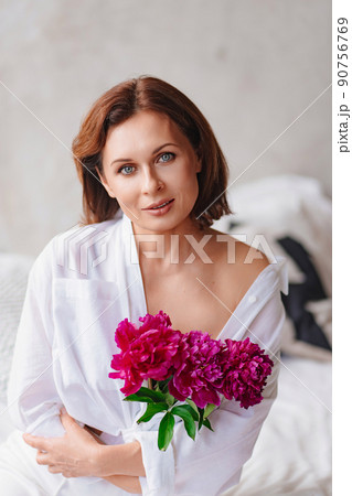 a gentle woman in white clothes with a peonies in the bedroom. home comfort. 90756769