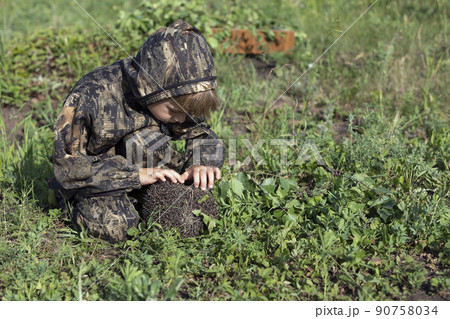 boy looks curiously at hedgehog caught in forest. Child with pet. 90758034