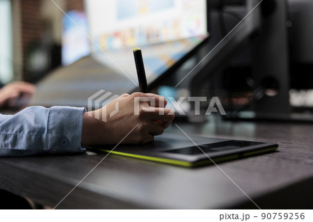 Closeup of creative graphic designer using stylus pen and graphic tablet to edit photos. Digital photo editor sitting at desk with multiple displays while using editing software to retouch images. 90759256
