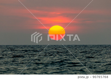 The sun is falling into the sea. , The sky is orange And the sea is dark 90765768