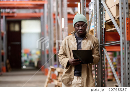Serious African worker looking at clipboard to check shipping shedule during hs work at warehouse Serious African worker looking at clipboard to check shipping shedule during hs work at warehouse 90768387