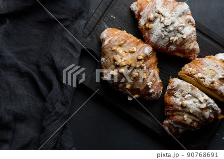 Baked croissant on a wooden board and sprinkled with powdered sugar, black table Baked croissant on a wooden board and sprinkled with powdered sugar, black table 90768691