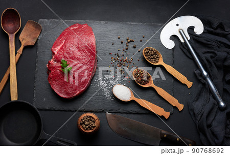 Raw beef tenderloin lies on a cutting board and spices for cooking on a black table Raw beef tenderloin lies on a cutting board and spices for cooking on a black table 90768692
