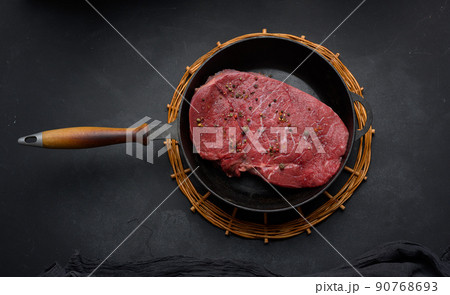 Raw beef tenderloin lies in a metal round frying pan on a black table Raw beef tenderloin lies in a metal round frying pan on a black table 90768693