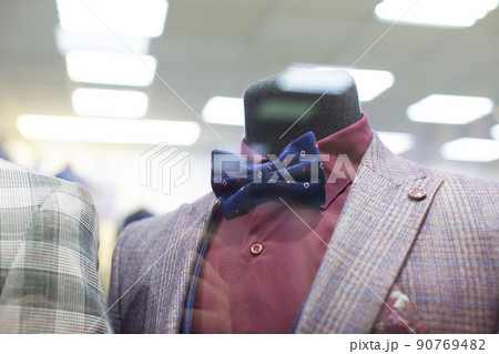 In the shop window is a mannequin in a formal suit and bow tie. 90769482