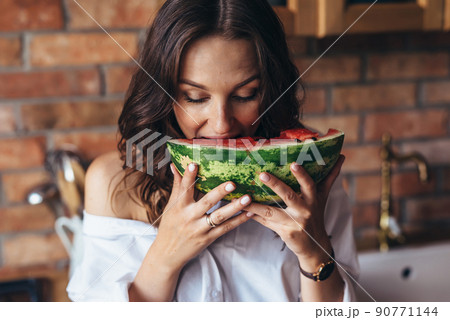 Woman at home eating watermelon in the kitchen Woman at home eating watermelon in the kitchen 90771144
