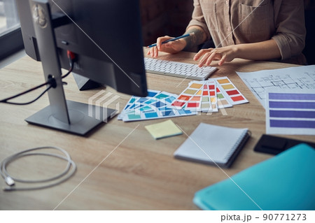 Female interior designer working on project of architecture drawing with color swatches, using computer at workplace Female interior designer working on project of architecture drawing with color swatches, using computer at workplace 90771273