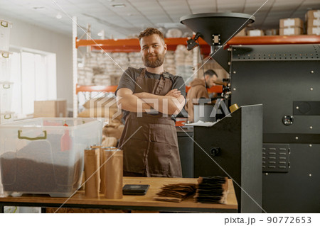 Portrait of smiling business owner on background of own small coffee factory looking camera Portrait of smiling business owner on background of own small coffee factory looking camera 90772653