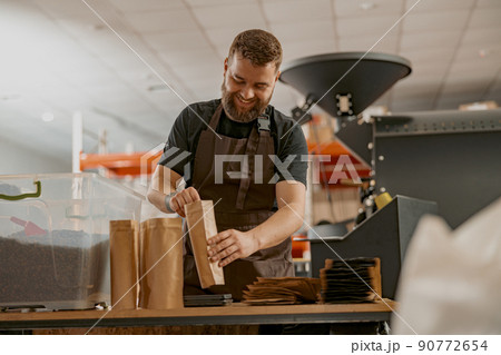 Business owner weighs paper bag with coffee beans on a scale at coffee factory Business owner weighs paper bag with coffee beans on a scale at coffee factory 90772654