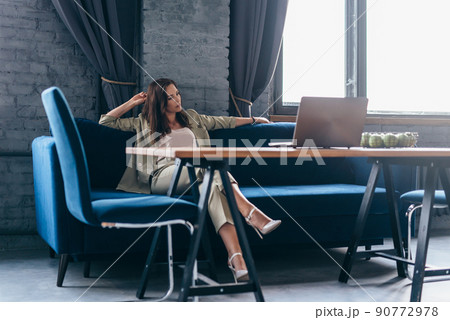 Woman at home sits relaxed on the couch and looks at her laptop screen 90772978