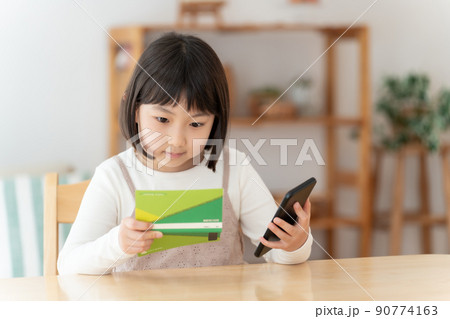 預金通帳とスマートフォンを見つめる女の子 90774163