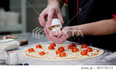 Restaurant kitchen. A chef putting special cheese on the pizza Restaurant kitchen. A chef putting special cheese on the pizza 90779215