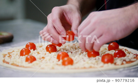 Restaurant kitchen. A chef putting cherry tomatoes on the pizza Restaurant kitchen. A chef putting cherry tomatoes on the pizza 90779216