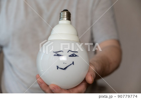 A middle-aged man is holding an electric lamp with his face painted on it. A happy smiling face is drawn in black marker. A large round electric lamp in the man's hand. Middle section of a mature man A middle-aged man is holding an electric lamp with his face painted on it. A happy smiling face is drawn in black marker. A large round electric lamp in the man's hand. Middle section of a mature man 90779774