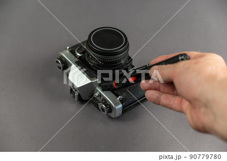 A middle-aged man cleans the dust off an analog camera. Special cleaning brush in a man's hand. Gray background. Selective focus. Indoor. 90779780