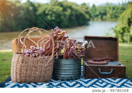 picnic set in the park near river, dried flowers, baskets wine bottle, book and retro gramophone vinyl record. Summer, spring and vacation concept picnic set in the park near river, dried flowers, baskets wine bottle, book and retro gramophone vinyl record. Summer, spring and vacation concept 90780168
