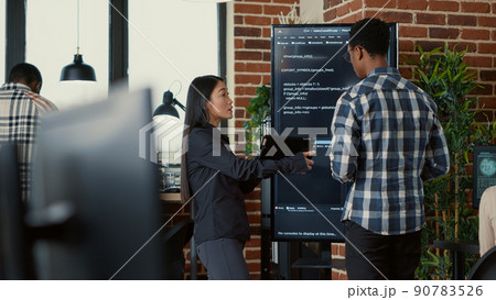 Team of coders analyzing code on wall screen tv comparing errors using digital tablet next to programer working with neural network. Software engineers collaborating on coding group project. 90783526