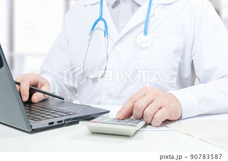 Doctor working with medical statistics and financial reports. doctor counts on calculator and enters data into laptop. male doctor using laptop and calculator at office 90783587