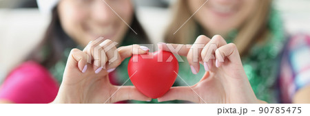 Sisters holding plastic red heart in hands and smiling Sisters holding plastic red heart in hands and smiling 90785475