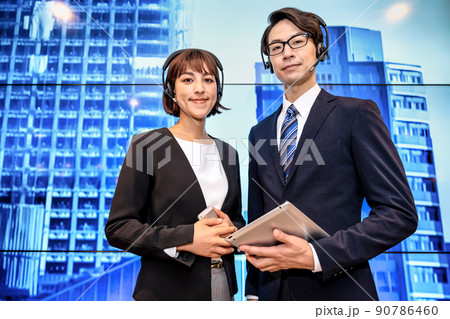 巨大ディスプレイの前で立ち話をするヘッドセットをしたビジネスウーマンとビジネスマン 90786460