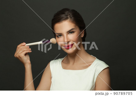 Close up beauty portrait of an attractive lovely young woman holding makeup blusher brush on black Close up beauty portrait of an attractive lovely young woman holding makeup blusher brush on black 90789705