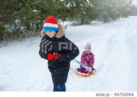 A teenage boy rolls a little girl in the snow on a plastic ice rink. A teenage boy rolls a little girl in the snow on a plastic ice rink. 90792068