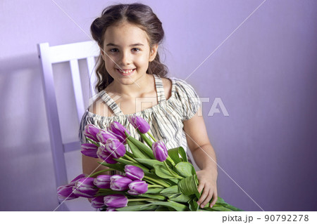 Beautiful little girl with a bouquet of tulips, against the background of a purple wall 90792278