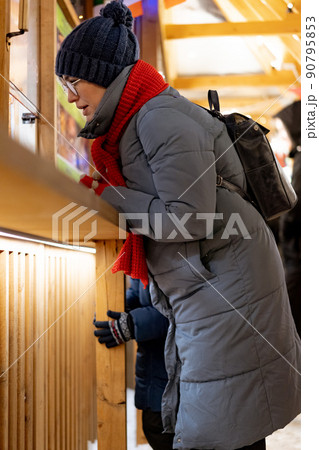 caucasian woman wearing hat and red scarf buying treats in kiosk at christmas market caucasian woman wearing hat and red scarf buying treats in kiosk at christmas market 90795853
