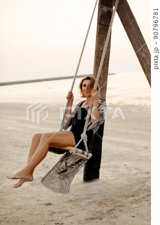 Romantic beautiful woman relaxing on a swing on the beach at sunset, summer vacation, travel and vacation vacation, inspiring landscape Romantic beautiful woman relaxing on a swing on the beach at sunset, summer vacation, travel and vacation vacation, inspiring landscape 90796781