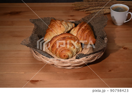 Freshly baked croissants in wicker basket and coffee cup on wooden tale. Breakfast, bread bakery products cafe concept 90798423