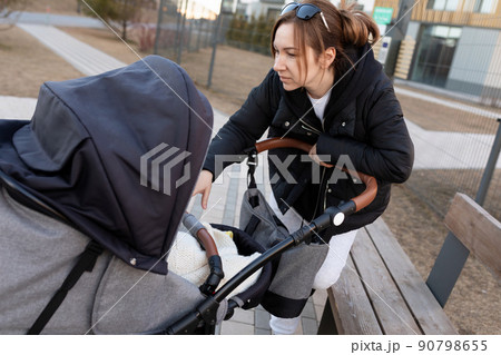 caring mother peeks into the pram while walking with her child 90798655