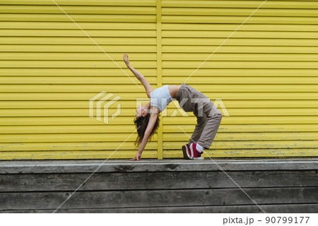 Young female in white top and linen pants dancing in front of yellow wall 90799177
