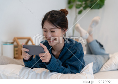 Closeup of asian woman playing online game on mobile phone on her bedroom. 90799211