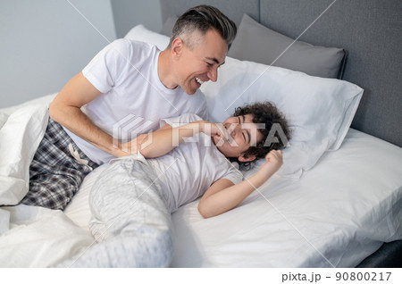 Father and son having fun in bed in the morning and looking joyful Father and son having fun in bed in the morning and looking joyful 90800217