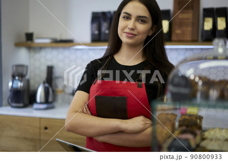 Positive prosperous woman waiter looking at camera near bar Positive prosperous woman waiter looking at camera near bar 90800933