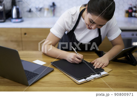 Skilled woman barista filling in invoice concentrated on numbers Skilled woman barista filling in invoice concentrated on numbers 90800971