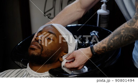 White-skinned guy hairdresser wipes his head with a towel to a stylish african guy 90801494