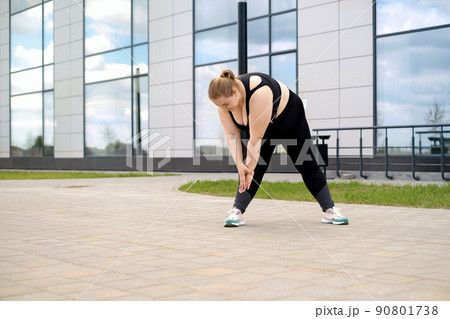 A young fat overweight woman does sports by stretching and bending forward on city streets 90801738