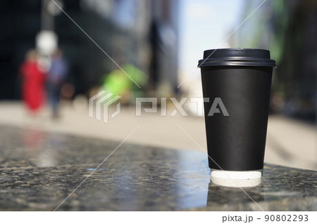 Takeaway coffee in a paper cup. Hot drink to go on the background of a busy city street. Paper cup mockup Takeaway coffee in a paper cup. Hot drink to go on the background of a busy city street. Paper cup mockup 90802293