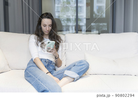 Young european woman using smartphone in home relaxed environment on sofa in free time. Internet, technology concept. 90802294