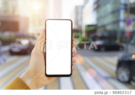 A smartphone in a hand with a blank screen against the backdrop of an urban street of the business quarter of the city. Business applications, transport, taxi, maps concept 90802317
