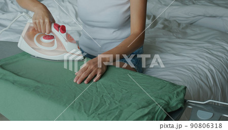 Woman iron clothes with iron on ironing board Woman iron clothes with iron on ironing board 90806318